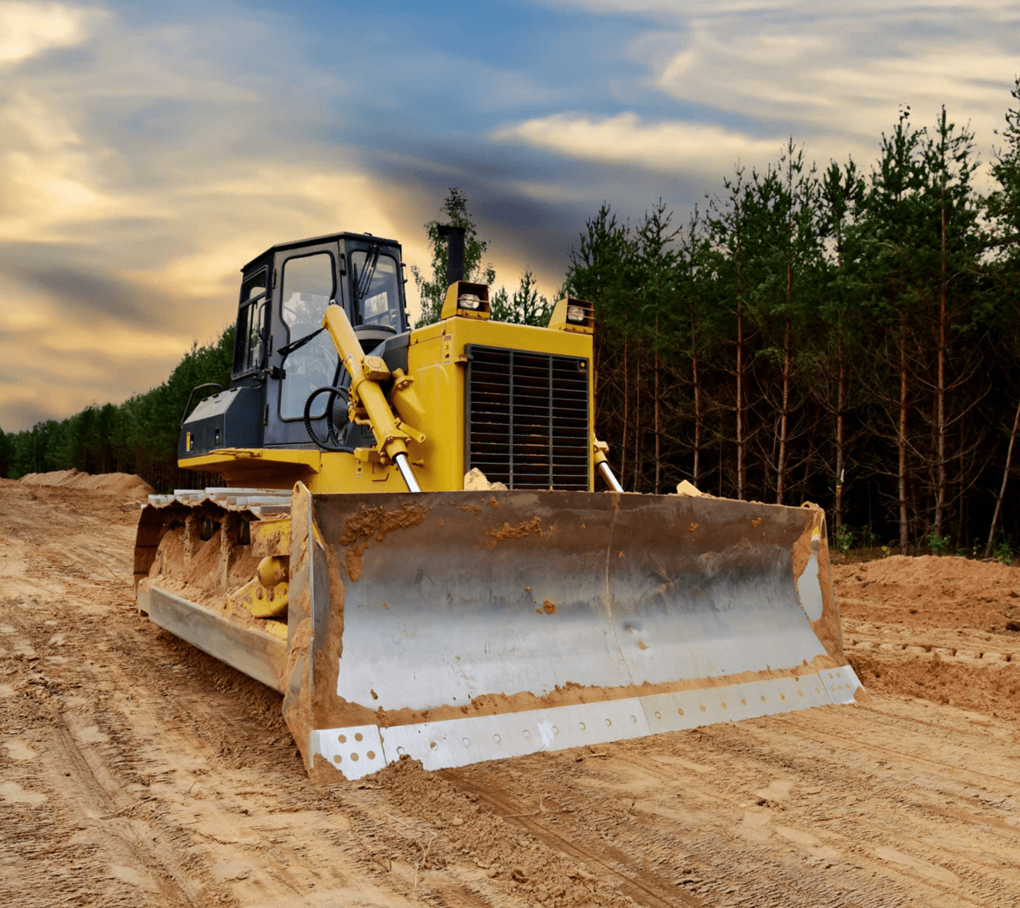 Bulldozer on dirt road near forest.